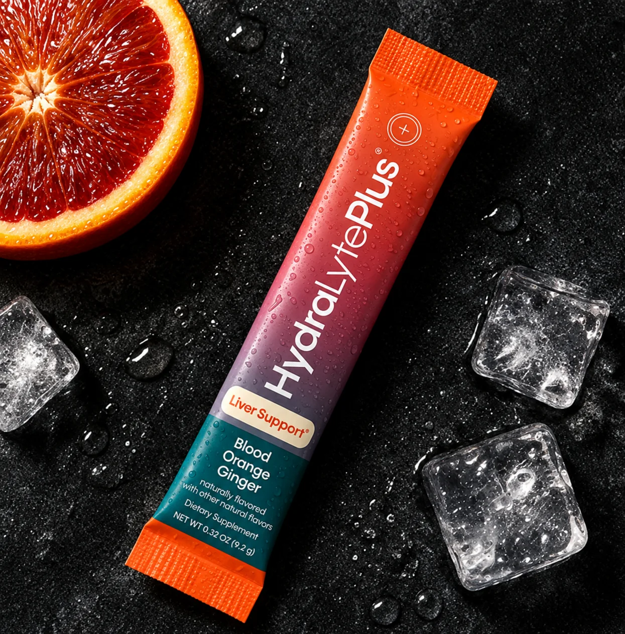 HydraLytePlus Blood Orange Ginger stick pack on dark stone with ice and blood orange