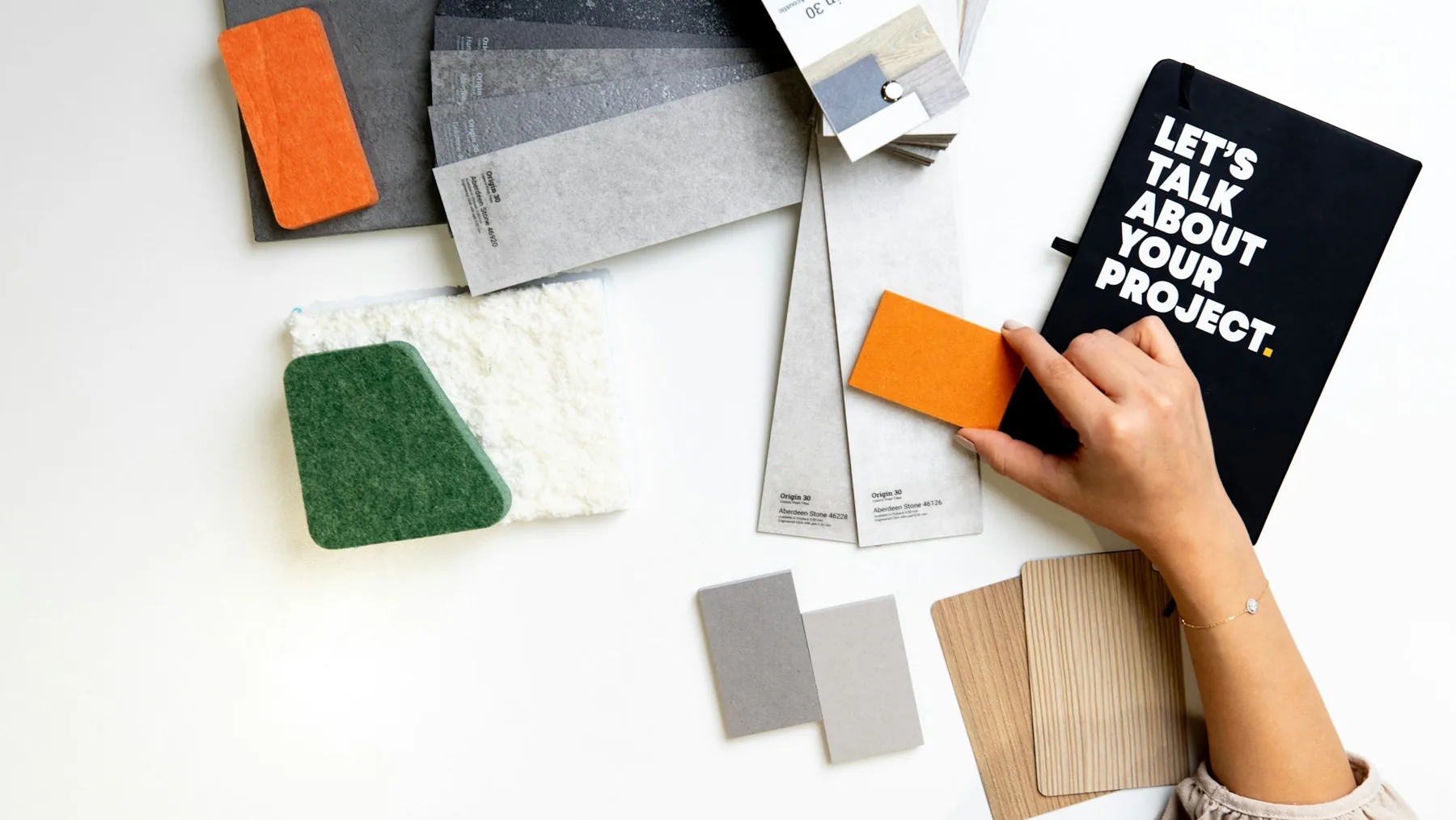 A designer’s hand choosing an orange material sample from swatches on a white desk